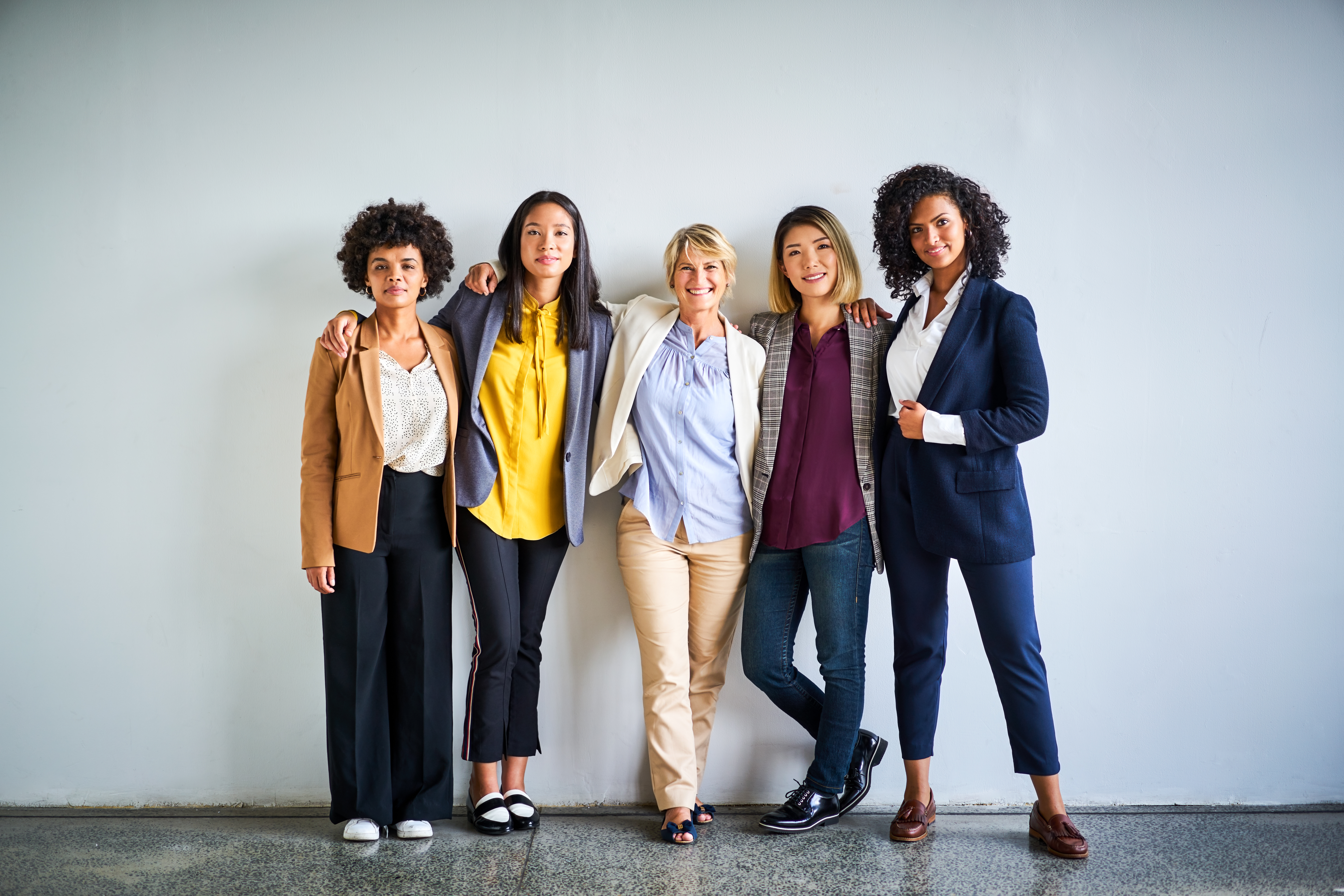 Portrait of confident female professionals. Smiling multi-ethnic businesswomen standing together. They are against wall at office.