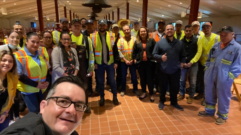 Group of workers in a semi circle, some wearing yellow reflective vests.