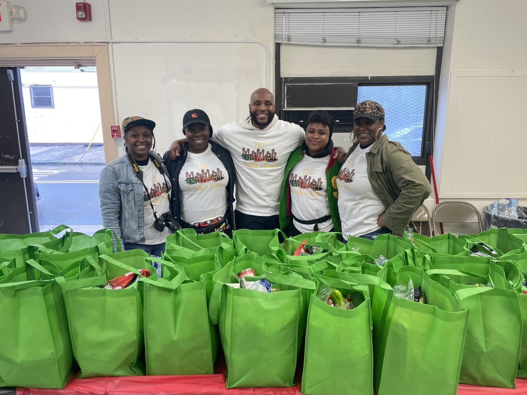 five people in front of green bags of food.
