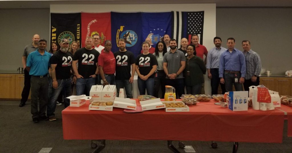 Group of people posing behind a table with food and military flags in the back.